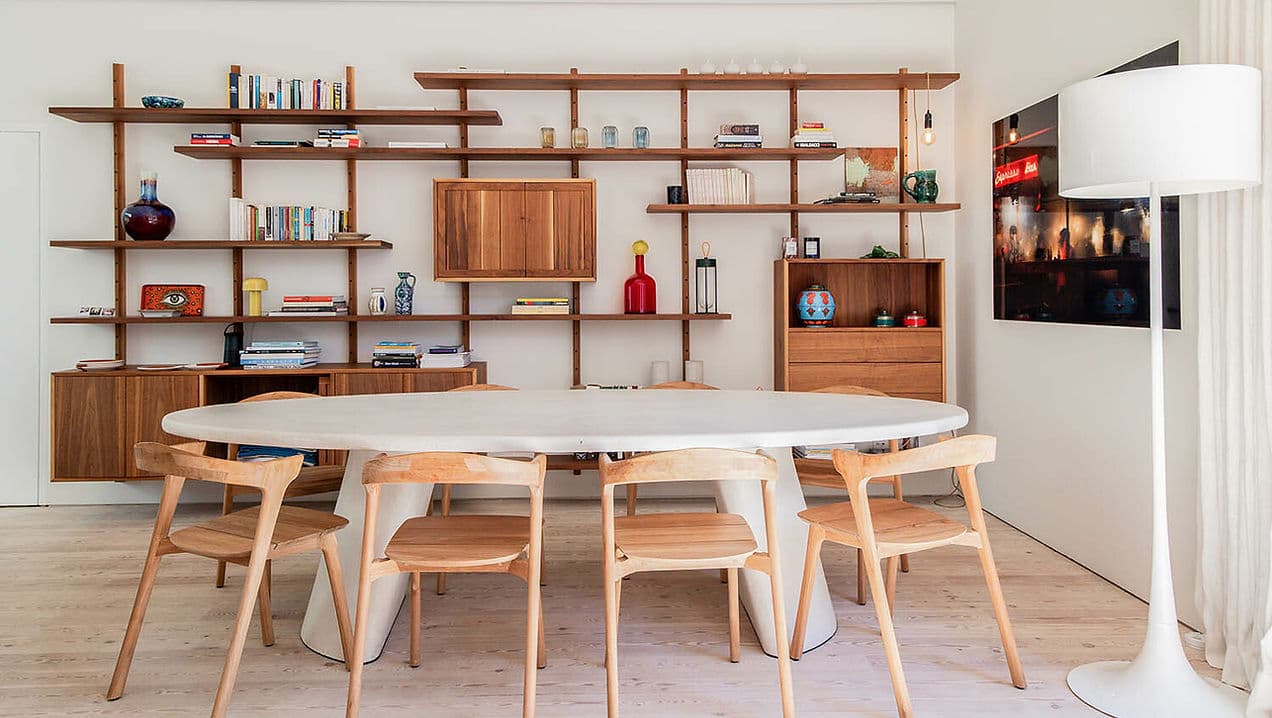 Dining area with oval table, wooden chairs, and wall shelving at Rafter Melides Atlantica in Melides, Portugal