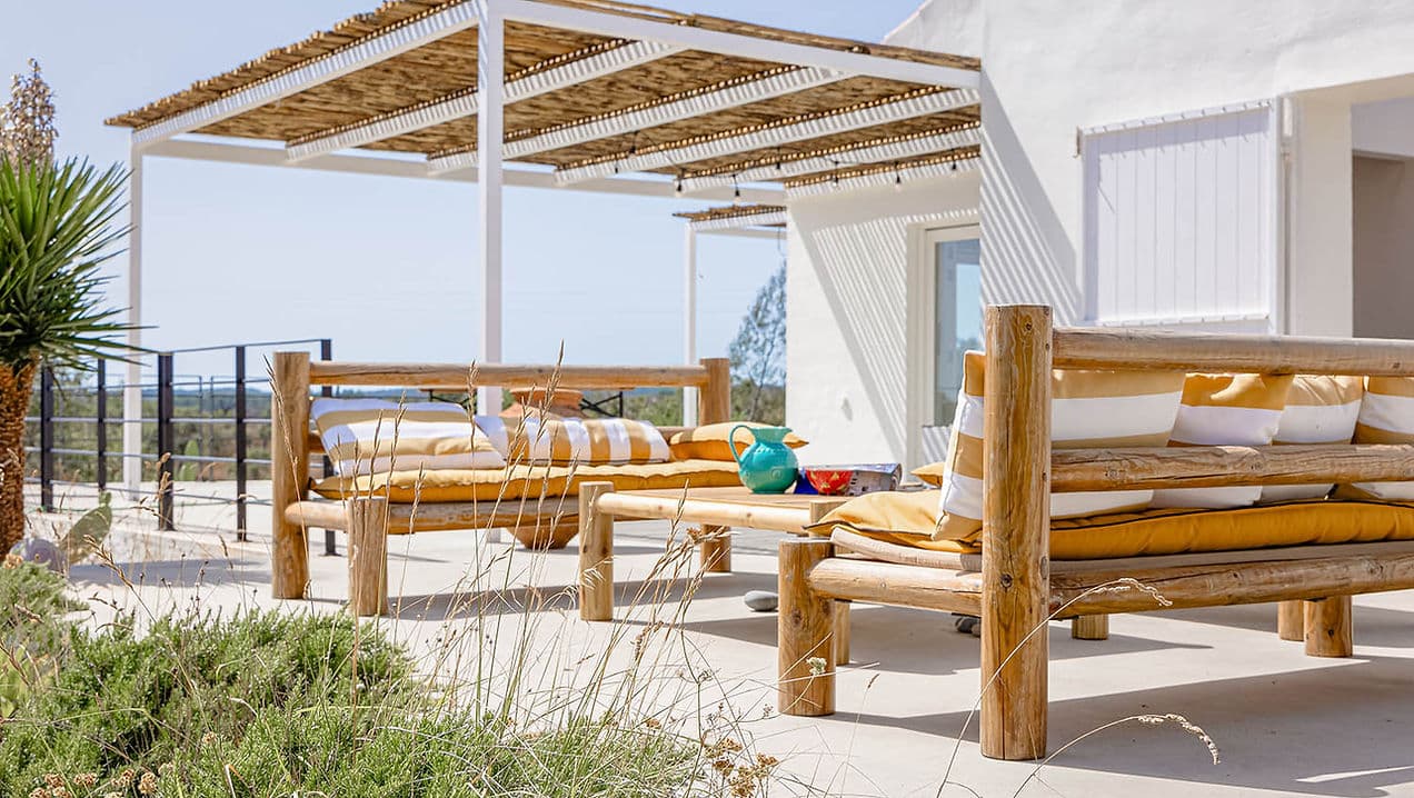 Outdoor lounge area with wooden furniture and shaded pergola at Casa Acima in Santiago do Cacém, Portugal