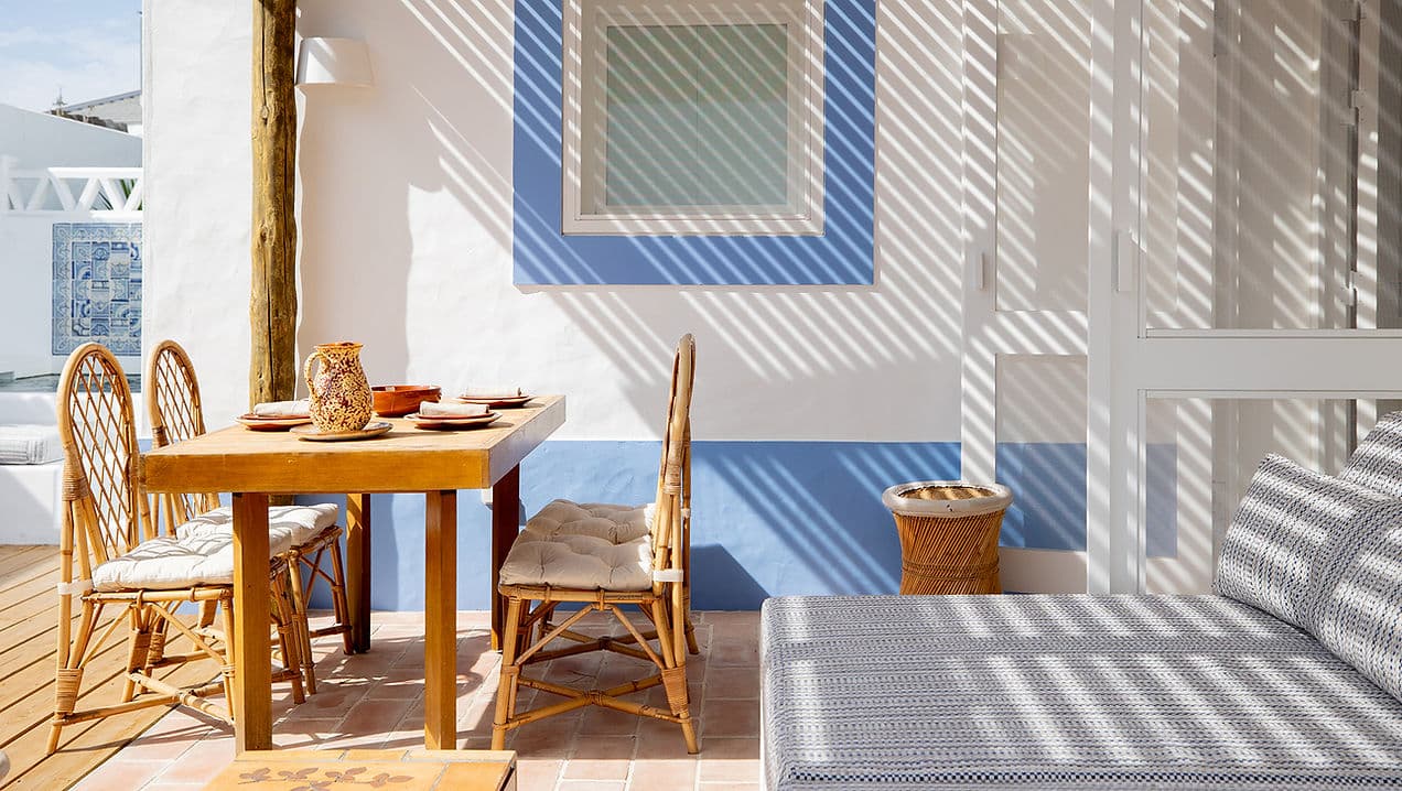 Outdoor dining area with rattan chairs and shaded seating at Casa Mounette in Portugal