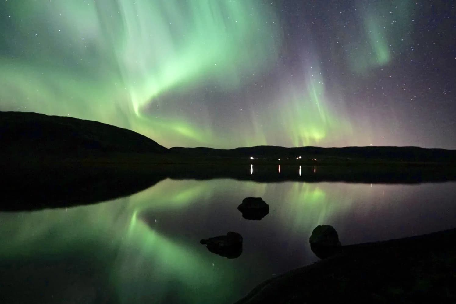 Northern lights reflecting over a calm lake near Rafter Aslundur in Iceland, natural light show view