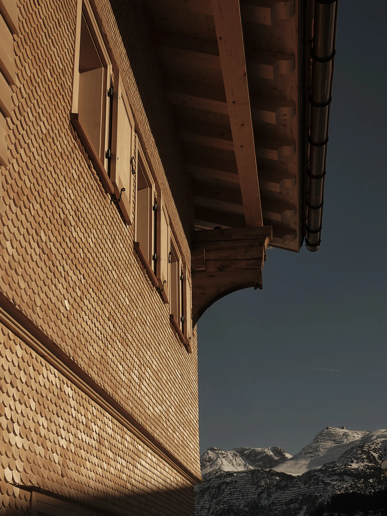 Exterior view of wooden wall and windows with alpine mountain backdrop at Rafter Lech Zug in Lech, Austria