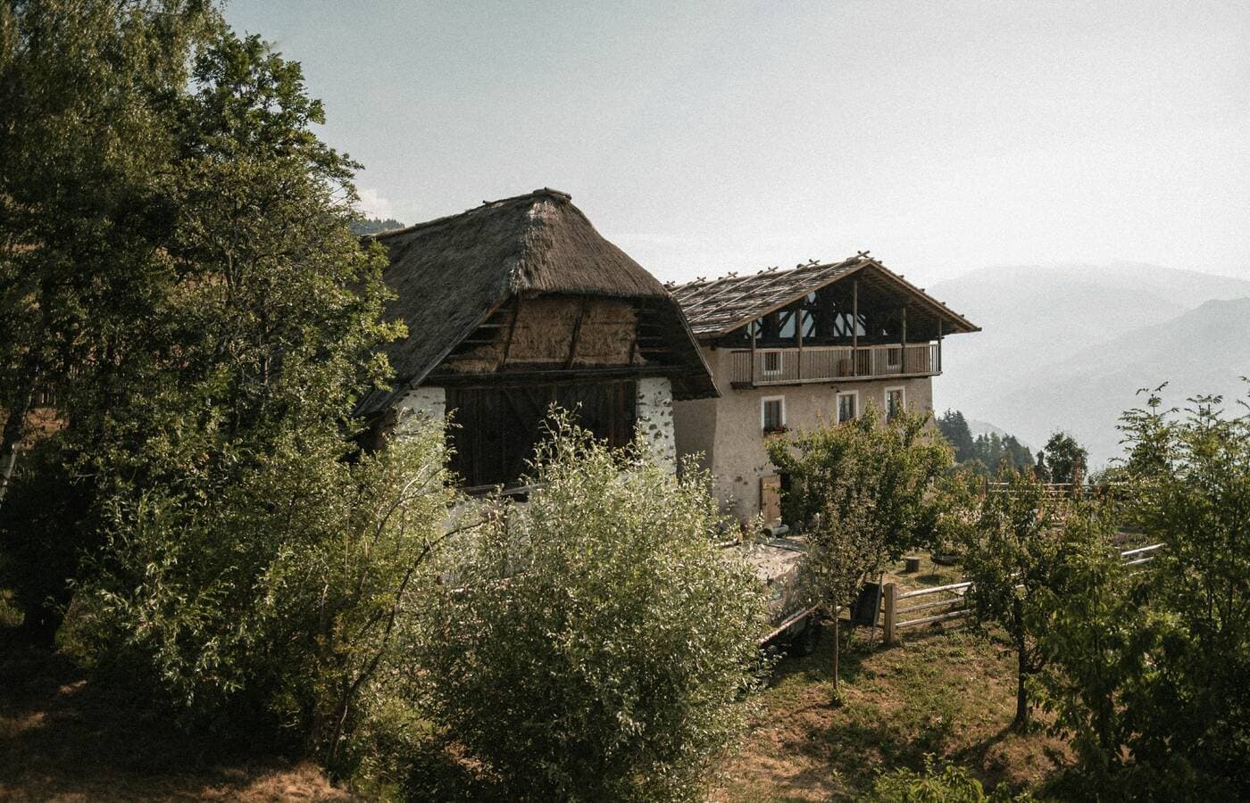 Traditional thatched roof building and modern balcony surrounded by trees at Rafter Villanders in Villanders, Italy with moun